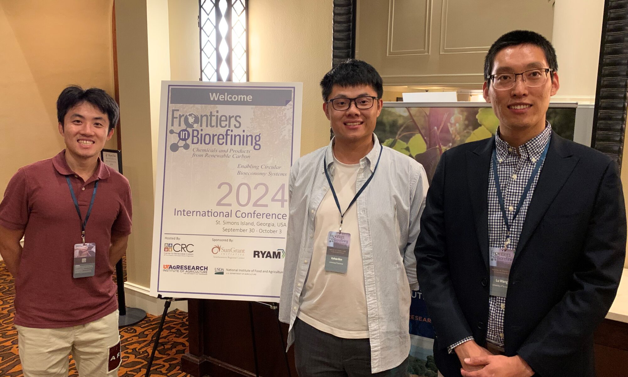 Xuan Li, Kehao Ren, Lu Wang stand in front of the conference logo.